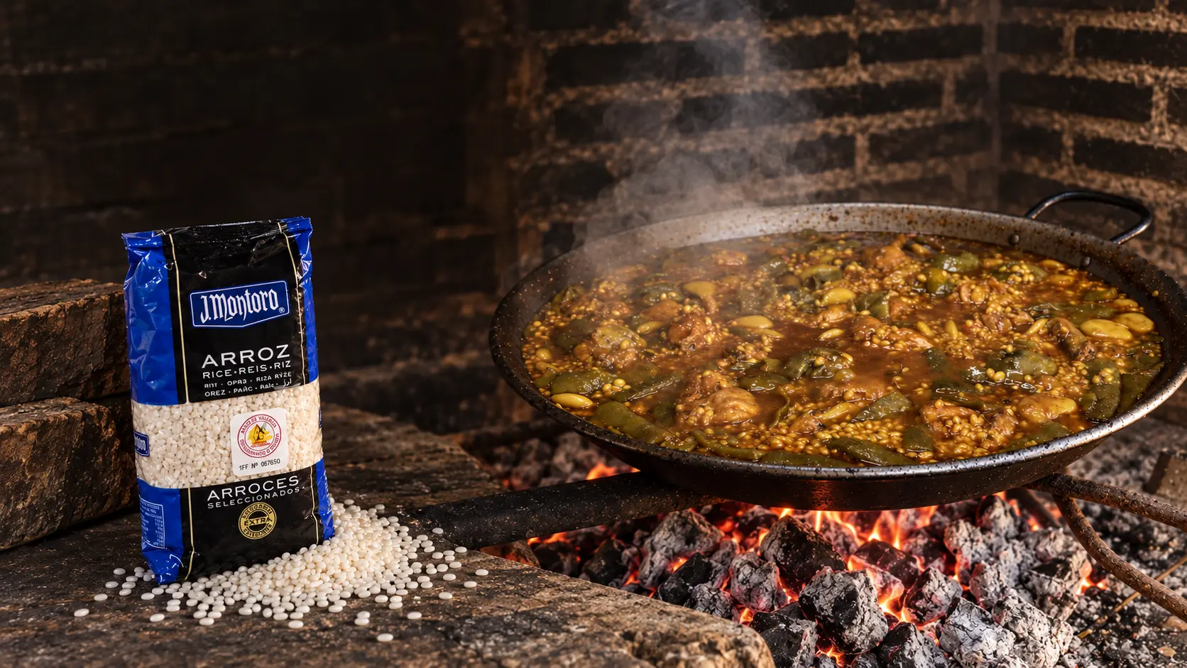 Paella cooking over embers beside a bag of J. Montoro rice
